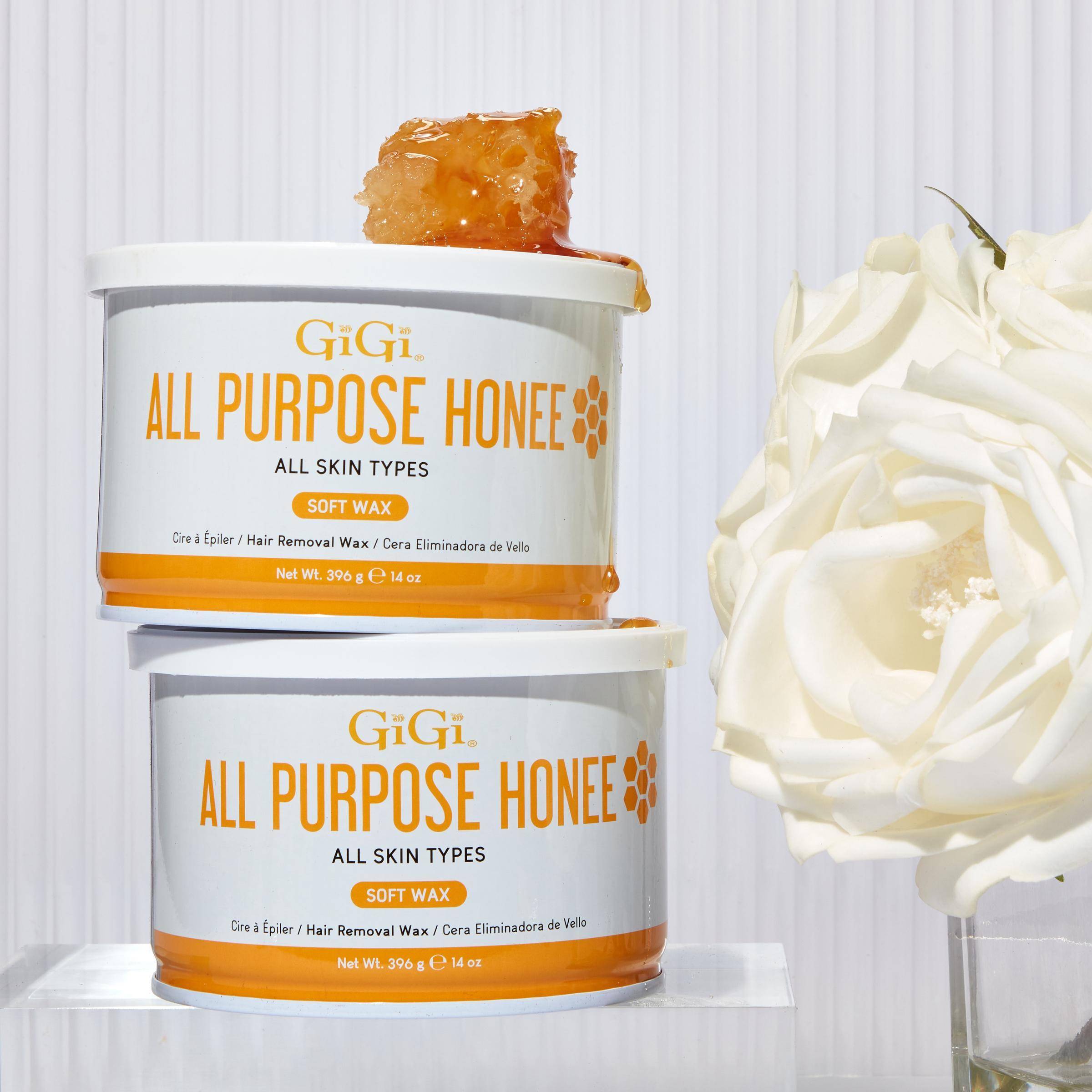 Two stacked containers of GiGi All Purpose Honee soft wax for hair removal,  placed beside a white rose on a clean