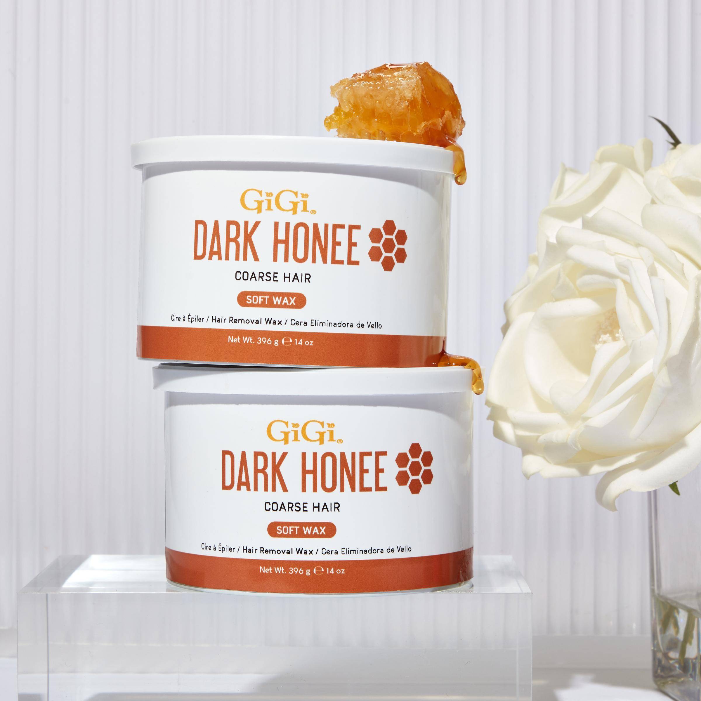 Two containers of GiGi Dark Honee soft wax on a white background with a white flower.