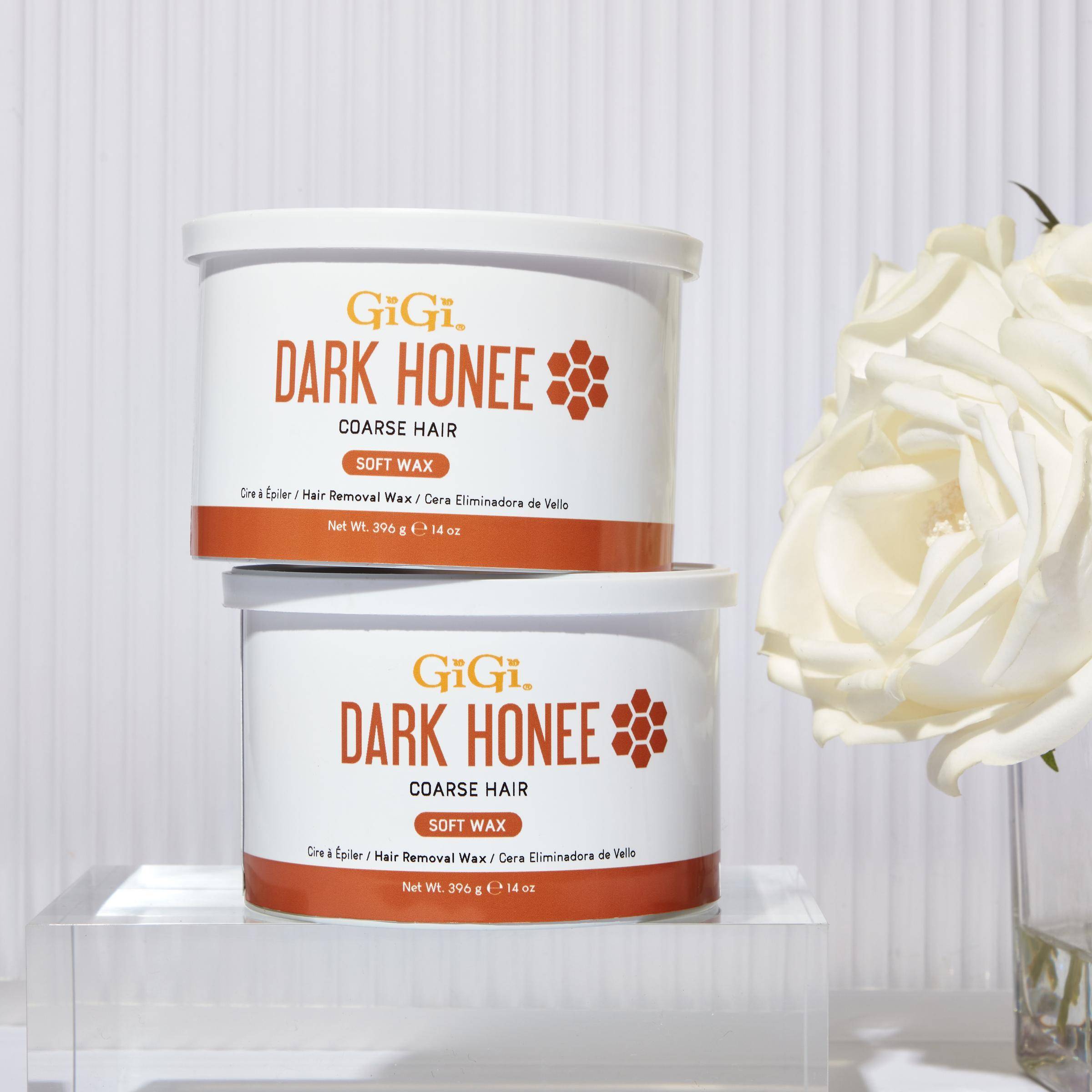 Two containers of GiGi Dark Honee soft wax for coarse hair on a white background with a white rose.